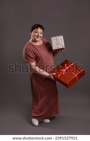 adult curvy woman full height holding gifts for Christmas on neutral monochrome grey background