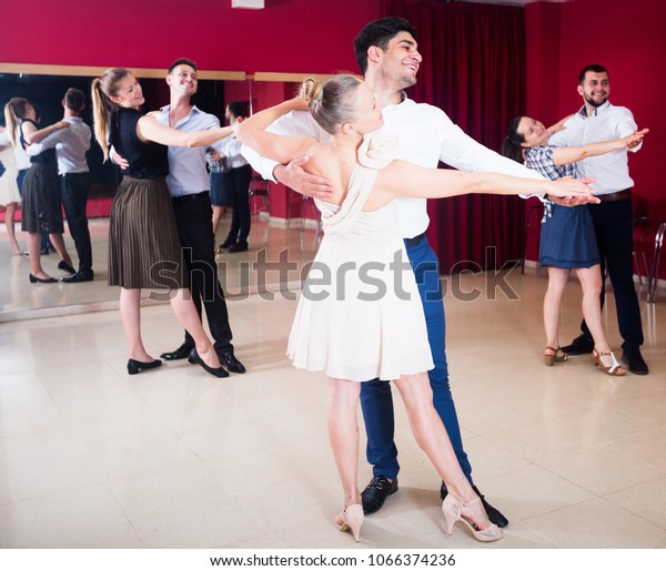 Adult\
dancing couples enjoying foxtrot in dance\
studio