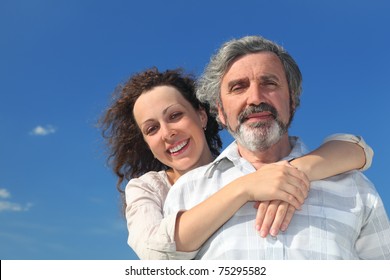 adult daughter embracing her father from back and smiling, blue sky