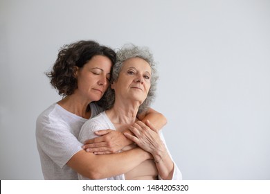 Adult Daughter Hugging Elderly Mother. Middle Aged Woman With Closed Eyes Hugging Thoughtful Senior Woman Standing Isolated On Grey Background. Emotion Concept