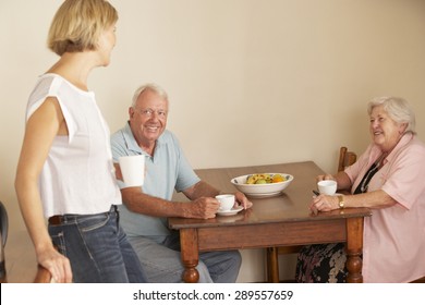 Adult Daughter Sharing Cup Of Tea With Senior Parents In Kitchen