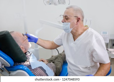 Adult dentist examines the oral cavity of his grandfather in a dental clinic - Shutterstock ID 1247048593