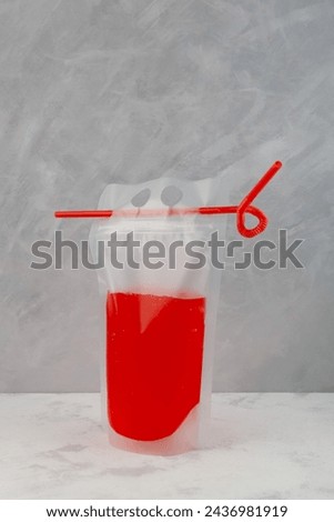 Adult drink in reusable pouch with drinking straw. Alcohol cocktail in plastic bag very convenient for picnics and gatherings. Red beer or fruit fermenting beverage.