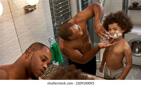 Adult Father Smearing Foam On Little Son Face And Teaching His Shaving At Home Bathroom. Domestic Family Lifestyle. Black Man And Child. Fatherhood And Parenting. Morning Time. Hygiene And Face Care