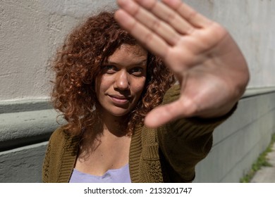 Adult female (34) Latin American afro-descendant curly hair with positive and doubtful attitude, extends the palm of her hand in front of the camera as a stop sign. Lifestyle concept. - Shutterstock ID 2133201747