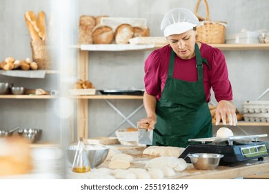 Adult female baker cutting dough with scraper and weighing pieces on scales - Powered by Shutterstock