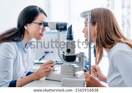 Adult female doctor ophthalmologist checking eye vision of young girl in modern clinic