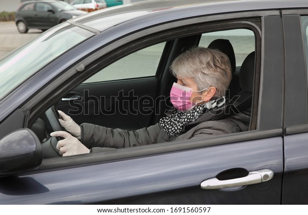 Adult female driver\
with protective surgical mask and gloves sitting in a car, corona\
virus protected person