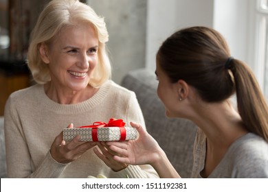 Adult female grownup child make birthday present greeting congratulating happy senior mother, smiling elderly 60 woman mom receive wrapped gift box with red bow, celebrating anniversary with family - Powered by Shutterstock