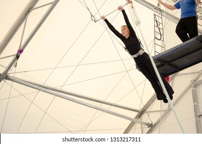 An Adult Female Hangs On A Flying Trapeze At An Indoor Gym. The Woman Is An Amateur Trapeze Artist.