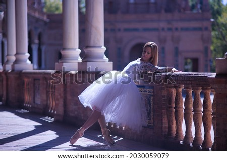 Adult female Hispanic classical ballet dancer making figures leaning on a stone balustrade, wearing a white tutu.
