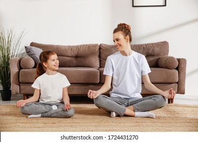 Adult female and little girl in similar sportive clothes sitting in lotus pose on floor in living and meditating together - Shutterstock ID 1724431270