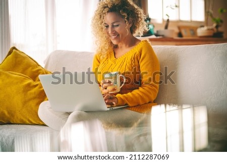 Adult female people using laptop computer at home smiling and enjoying connection technology sitting on the sofa. Hapy woman enjoy online modern lifestyle and surf the web