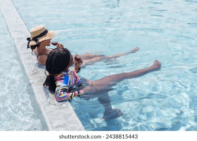 Adult female with straw hat and child with braids sit by pool edge, sharing moment and red wine glasses, familial bond and leisure. Grown woman in sunhat and young individual with plaited hair  - Powered by Shutterstock