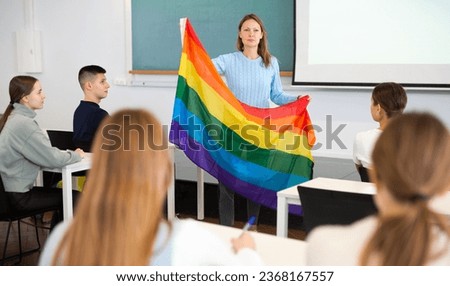 Adult female teacher in classroom showing LGBT flag to students in class