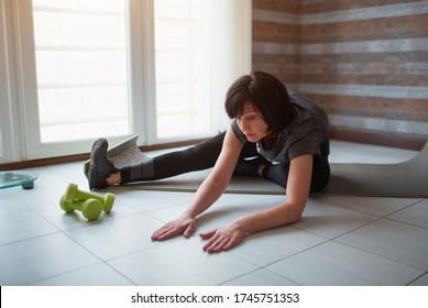 Adult fit slim woman has workout at home. She is doing stretching on a yoga mat by the window Take care about body - Shutterstock ID 1745751353