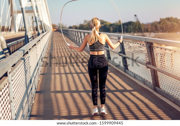 Adult fitness woman\
skipping the rope on the bridge at sunset. Fitness, sport and\
healthy lifestyle\
concept.