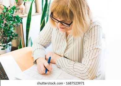 Adult Focused Blonde Woman In Glasses Using Laptop, Writing Notes In Workplace At Home. Remote Training, Learning. Female Watching Webinar. Online Education And Distance Work Concept