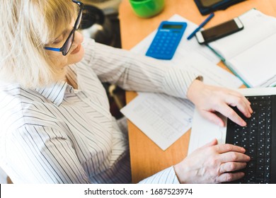 Adult Focused Blonde Woman In Glasses Using Laptop, Writing Notes In Workplace At Home. Remote Training, Learning. Female Watching Webinar. Online Education And Distance Work Concept