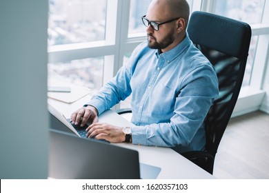 Adult focused businessman in glasses sitting in armchair at office desk and working on modern tablet while typing on portable keyboard - Shutterstock ID 1620357103