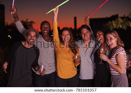 Adult friends waving glowsticks at rooftop party in Brooklyn