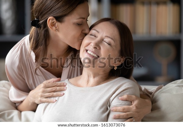Adult girl child kiss overjoyed middle-aged mom
relaxing together on sofa in living room, happy grownup daughter
rest enjoy time at home with senior mother, showing love and care,
bonding concept