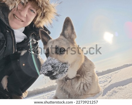 Adult girl or middle aged woman in a jacket with fluffy fur hood with shepherd dog in nature in winter on cold sunny day