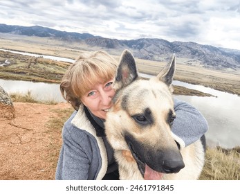 Adult girl with shepherd dog taking selfie near water of lake or river in mountain. Middle aged woman and big pet on nature. Friendship, love and fun - Powered by Shutterstock