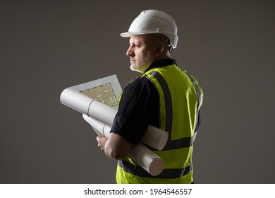 Adult gloomy builder. Portrait builder with his back to camera. He holds architectural drawings in his hands and looks away. Experienced builder in yellow vest. Concept sale of construction uniforms