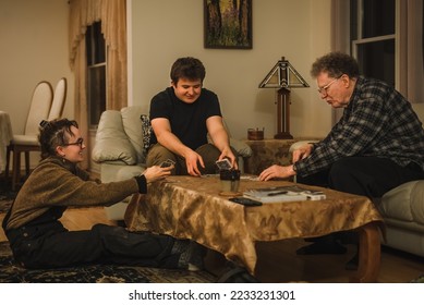 Adult grandchildren playing cards with their senior grandfather in  living room in evening - Powered by Shutterstock