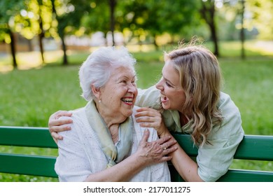 Adult granddaguhter helping her grandmother to use cellphone when sitting on bench in park in summer. - Powered by Shutterstock