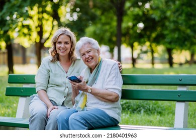 Adult granddaguhter helping her grandmother to use cellphone when sitting on bench in park in summer. - Powered by Shutterstock