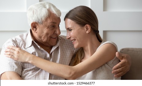 Adult Granddaughter And 80s Grandfather Embracing Sitting On Couch At Home, Multi-generational European People Having Good Warm Relations, Love And Care Of Elderly Father And Grown Up Daughter Concept