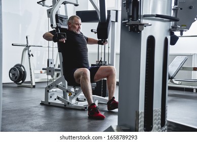 Adult Gray-haired Man Trains On Fitness Equipment In The Gym, Pumps Legs And Arms Muscles, Loses Weight. Concept Of Healthy Lifestyle In Old Age