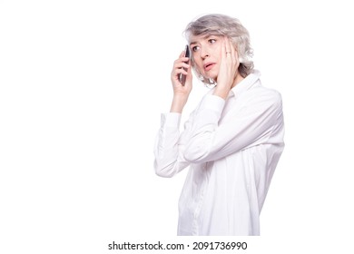 An Adult Gray-haired Woman Looks Scared And Upset, Holding Her Head While Talking On A Mobile Phone Isolated On White Background. Phone Fraud