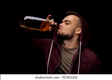 An Adult Guy Is Drinking An Alcoholic Drink From A Large Bottle On A Saturated Black Background. A Sad And Depressed Guy Is Addicted To Alcohol. Alcoholism Concept. Copy Space. 