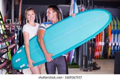 Adult guy with girl who are buying surfboard in store in time summer holidays - Shutterstock ID 1609367557