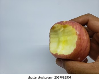 adult hand holding a red apple with bite marks on a white background