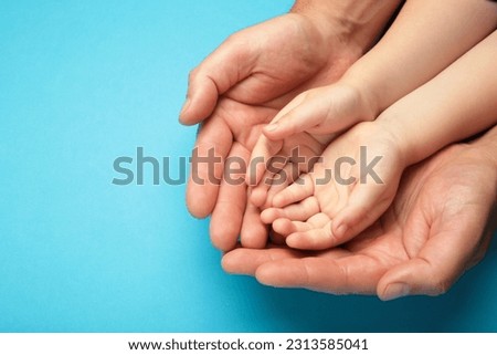 Adult hands holding kid hands, Family Help Care Concept, small hands in fathers hand on blue background. Top view