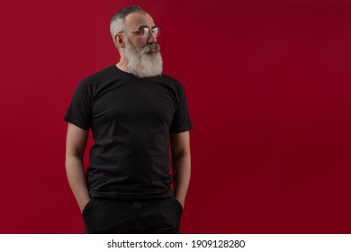 Adult handsome senior male model with a gray beard wearing a black t-shirt. Front view. Mock up space for your logo or design over dark red isolated background