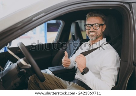 Adult happy fun man customer male buyer client wear shirt drive electric car with seat belt choose auto want to buy new automobile in showroom vehicle salon dealership store motor show. Sales concept