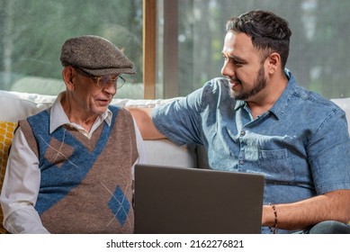 Adult and happy older father next to his adult son having a relaxed conversation enjoying the moment together in the comfort of their home. Two generations father and son.