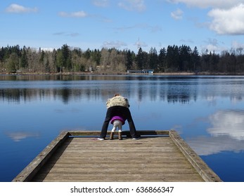 Adult Helps Child Peer Over The Edge Of A Dock On A Lake.