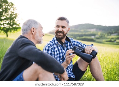 An adult hipster son with binoculars and senior father sitting on the grass in sunny nature. - Powered by Shutterstock