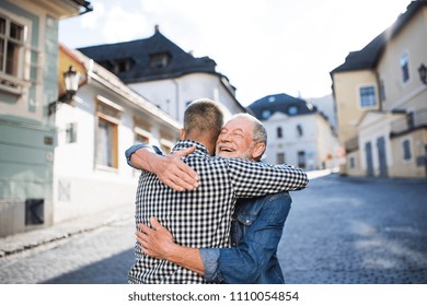 An adult hipster son and his senior father in town, hugging.