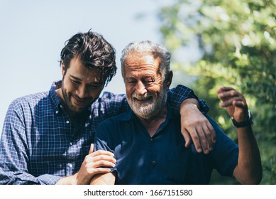 An adult hipster son and senior father at home, talking and smiling with family together, social distancing lockdown and work from home concept - Shutterstock ID 1667151580