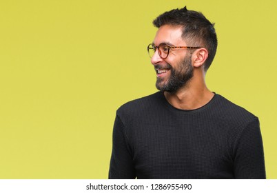 Adult hispanic man wearing glasses over isolated background looking away to side with smile on face, natural expression. Laughing confident.