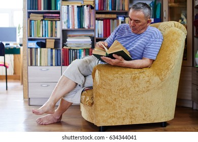 An Adult Kazakh Reads A Book Sitting In His Home Library