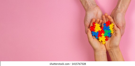 Adult And Kid Hands Holding Colorful Heart On Light Pink Background. World Autism Awareness Day Concept