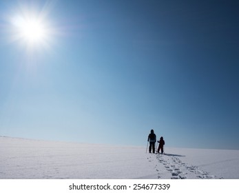 Adult And Kid Snowshoeing In The Sunlight